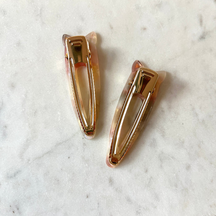 Two gold hair clips on a marble surface