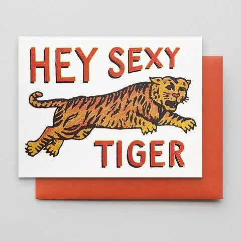 A square greeting card with a white front featuring the words โHEY SEXY TIGERโ in red-orange lettering and an illustrated tiger in orange, yellow, and black, shown with a matching orange-red envelope behind it on a light gray background.