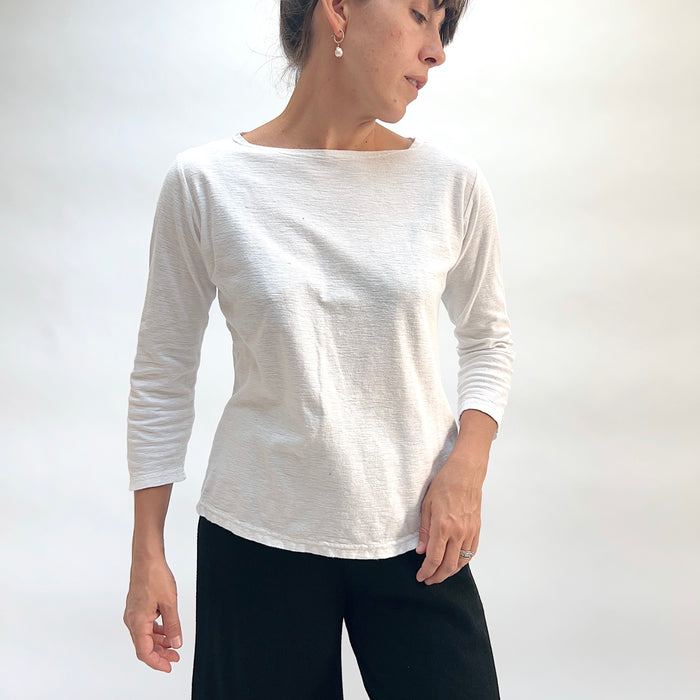Model wearing the Cut Loose 3/4 Sleeve Boatneck Top in White, three-quarter front view looking down, white cotton-linen boatneck top with wide neckline, 3/4 sleeves, and relaxed straight hem, styled with black pants