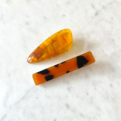 Two amber-colored hair clips with black spots on a white marble surface