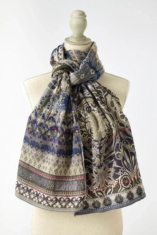 Létol Anoushka Scarf in Jean Trellis, draped and knotted on a linen dress form against a light grey background, showing a reversible Jacquard-woven organic cotton scarf — one side featuring a dense blue and oatmeal floral and trellis pattern with small repeated botanical motifs, the other showing large khaki and oatmeal Mughal medallion and palm tree scrollwork on a taupe ground — with the woven Létol label at the lower center and a pink accent selvedge visible at the hem