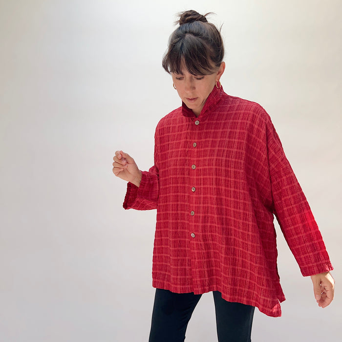 Eleven Stitch Big Shirt in Stripe Crinkle Ruby, three-quarter front view on model looking down, ruby red crinkle stripe rayon-nylon with stand collar, five wood button closure, wide dropped sleeves, and A-line hem, paired with black slim trousers