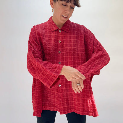 Eleven Stitch Big Shirt in Stripe Crinkle Ruby, front view on smiling model adjusting cuffs, showing point collar, five wood button closure, crinkle stripe texture in ruby, and relaxed oversized fit, paired with dark slim trousers