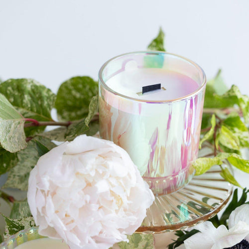 Iridescent candle with black wood wick in Stacy K's signature scent close up with blooms.