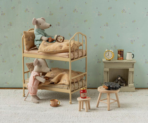 Maileg Bunk Bed in Wheat — lifestyle scene of two Maileg mouse dolls in a cosy bedroom, one in a teal top resting on the top bunk with a waffle and honey jar, one in a pink romper standing at the lower bunk holding a tea tray, beside a miniature fireplace and wooden stools