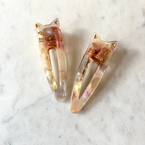 Two cat-shaped hair clips on a marble surface