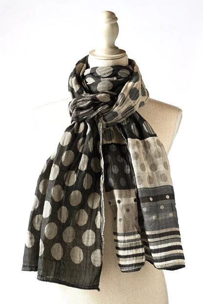 Létol Coline Scarf in Noir Gris, draped and knotted on a linen dress form against a white background, showing a reversible Jacquard-woven organic cotton scarf — one side featuring large oatmeal and beige polka dots on a deep black ground, the other showing a light chambray and beige ground with smaller dots and a bold black and grey striped border — with the fringe edge visible at the hem