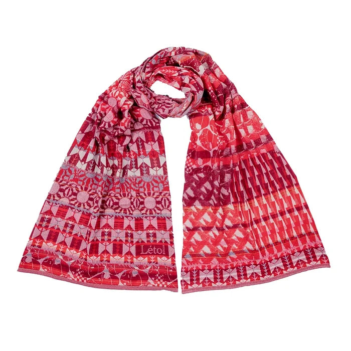Létol Come Scarf in Red Gala, draped and loosely knotted against a white background, showing a reversible Jacquard-woven organic cotton scarf with rich red, cranberry, and pink tones featuring geometric and floral motifs on one side and an abstract striped pattern on the other, with a woven Létol label visible at the border
