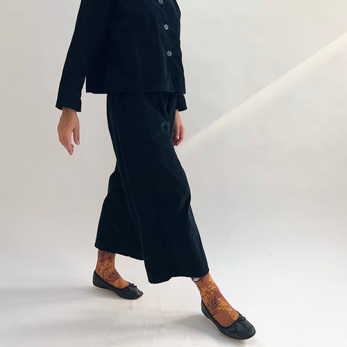 Model in motion wearing the Bryn Walker Corduroy Flood Pants in Black, side view highlighting wide-leg drape, flood-length hem, and black pinwheel corduroy texture, paired with matching Standing Collar Crop Jacket, printed socks, and black ballet flats
