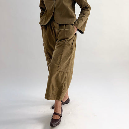 Model with hand on hip wearing the Bryn Walker Corduroy Pasha Pants in Partridge, front view showing side leg patch pockets, elastic waistband, and olive pinwheel corduroy, paired with matching Audrey Jacket and dark Mary Jane flats