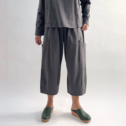 Model wearing the Bryn Walker Cotton Pasha Pant in Moonlight, full front view showing elastic gathered waistband, two large thigh patch pockets, wide-leg cropped length, and soft blue-grey cotton, styled with matching top and green wedge clogs