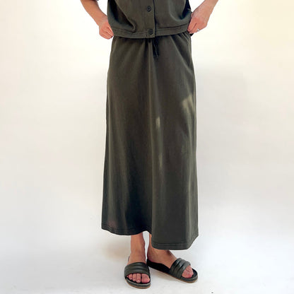 Person wearing a long dark green skirt and top on a white background