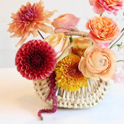 fall basket with orange dahlias, bronze mums, ranunculus, marigolds, light pink sweet pea, and peach roses close up.