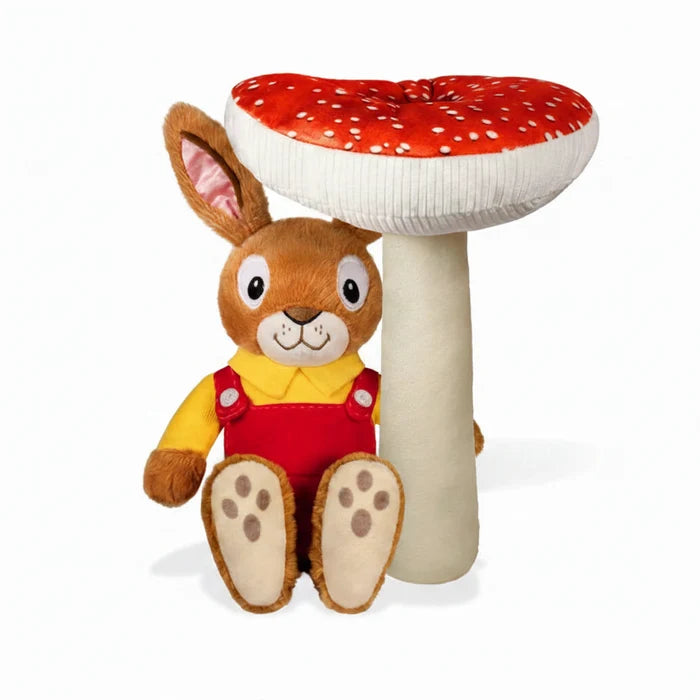 Nicholas bunny plush toy seated in front of a red-and-white spotted toadstool. The soft toy wears red overalls and a yellow shirt, with embroidered facial features, against a white background.