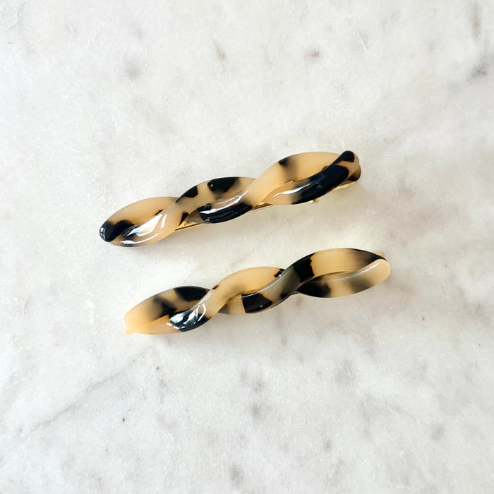Two tortoiseshell hair clips on a marble surface