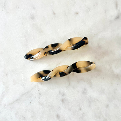 Two tortoiseshell hair clips on a marble surface
