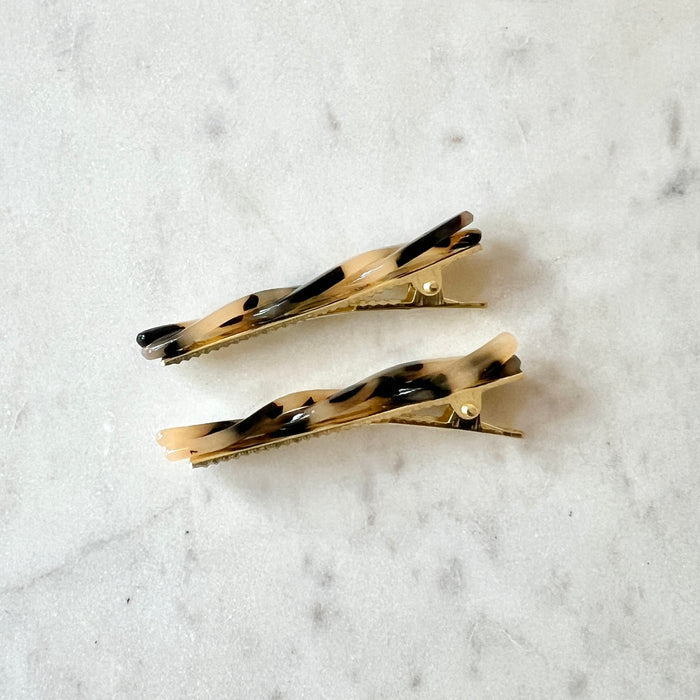 Two tortoiseshell patterned hair clips viewed from the side on a light marble background