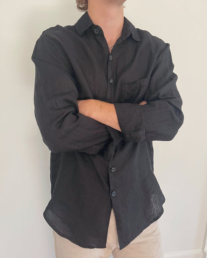 Model wearing Two Sons black linen button down shirt with arms crossed, styled with beige trousers