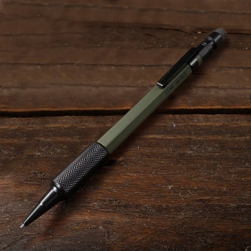 An olive green and black mechanical pencil resting diagonally on a dark brown wooden surface.