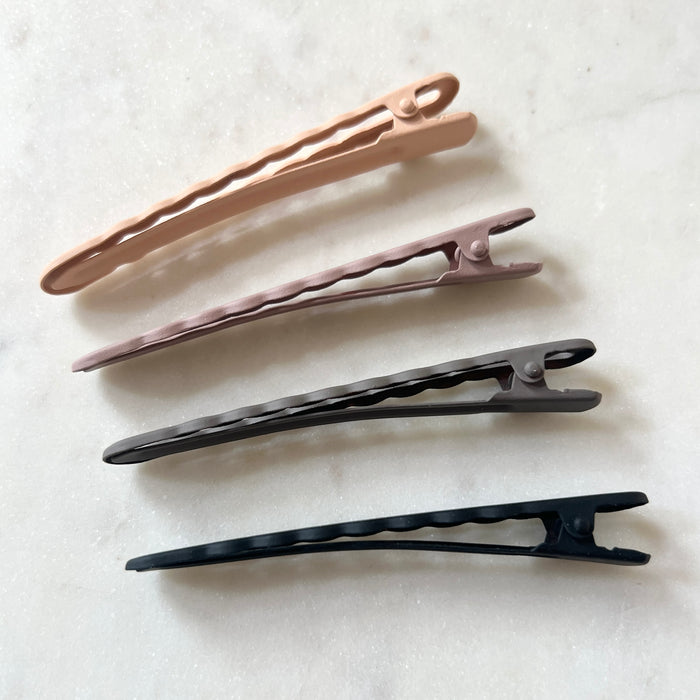 Set of four hair clips in beige, pink, black, and dark gray on a light background