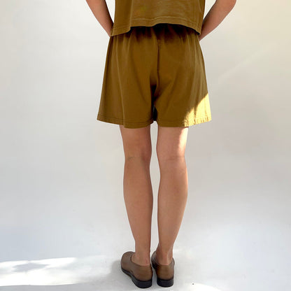 Person wearing a brown outfit with shorts and a top on a white background, viewed from the back