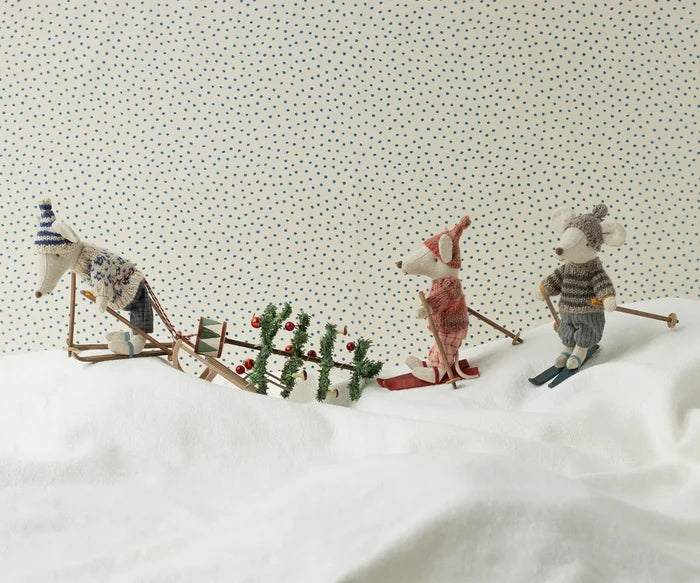 Maileg Winter Mouse Ski Dad — lifestyle scene of three Maileg mouse dolls in winter ski outfits on a snowy white surface, with a miniature sled, Christmas tree, and holiday accessories